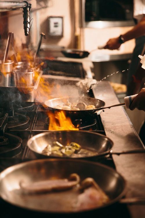 Cucina a vista di Vesper Milano con padelle in fiamma durante il servizio del pranzo in zona Isola