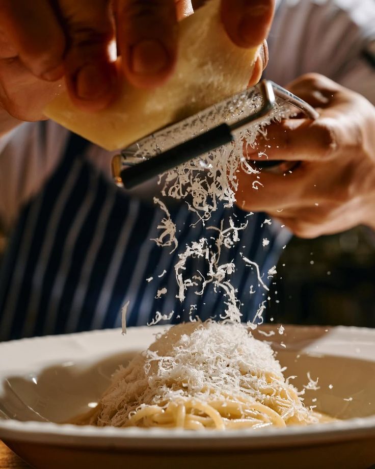 Grattugia di parmigiano reggiano sopra un piatto di pasta lunga, pranzo tradizionale italiano da Vesper Milano