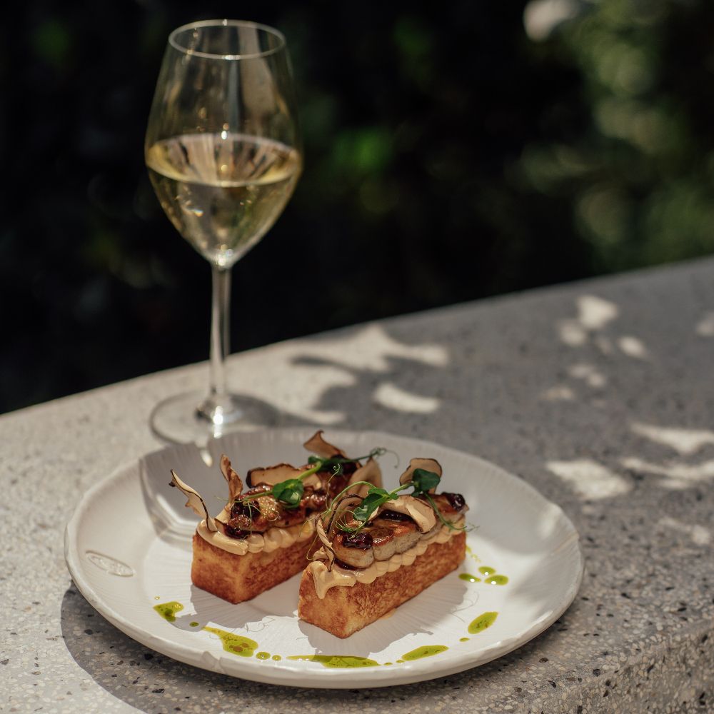 Crostini gourmet con foie gras e funghi porcini accompagnati da un calice di vino bianco per l'aperitivo da Vesper Milano